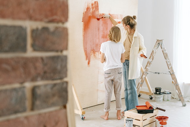 Parent and child painting a white wall orange while surrounded by painting materials